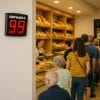 Display eliminacode digitale a muro in panificio con clienti in fila