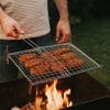 Griglia barbecue cromata con carne in cottura su brace viva, uso esterno