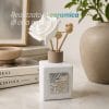 profumatore comunione materiale Diffusore di profumo in ceramica bianca con rosa decorativa e dettagli religiosi, appoggiato su superficie con elementi d’arredo.
